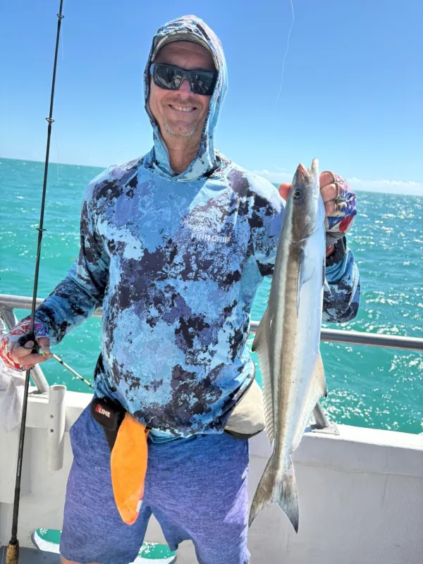 Person in camo hoodie holding a fish on a boat with the ocean in the background.